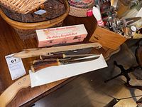 Overview of kitchen utensils including boxed rotary spaghetti fork, knives with stag handles, cutting utensils in baskets, and other metal kitchen tools