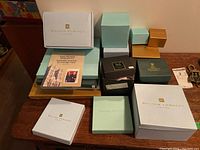 Multiple boxed items on table from William Edwards including collector plates, teacups, and a certificate booklet.