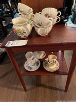 Collection of Copeland Spode teacups and saucers along with a floral pitcher and bowls arranged on a wooden side table.