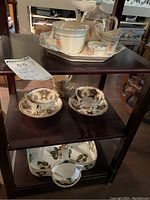 Photo shows the three shelves with all tea set items including two Paragon teacups with saucers, Hammersley caddy with creamer and sugar bowl on top shelf, Royal Windsor Gremwades tray and creamer on bottom shelf.