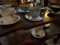 Overview of multiple teacups and saucers on a wooden table with varied floral and classic patterns.