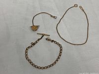 Three vintage pocket watch chains displayed on a white fabric background, showing a gold filled chain, brass chains, and a decorative fob.