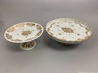 Front view of both porcelain pedestal serving dishes showing gold floral hand-painted designs on white base.