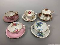 Image showing all five bone china teacup and saucer sets arranged on grey background, various floral patterns and gold trimming visible.