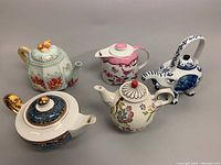 Top view of all five assorted vintage ceramic teapots showing variety of shapes, colors, and styles