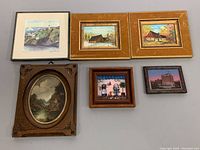 Six assorted framed artworks laid out on table including oil paintings, watercolor, and small images. Frames show signs of wear.