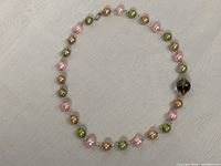 Full view of the necklace laid out in a circular form showing the sequence of pink, green, and golden pearls and centerpiece smoky quartz bead.