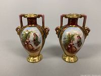 Front side of both miniature Royal Vienna porcelain urns showing hand painted classical scenes and gold accents.
