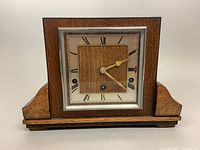 Front view of rectangular wooden mantle clock with Art Deco design, square face with Roman numerals and metal trim around glass cover.