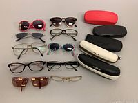 Overview of 11 assorted pairs of glasses and sunglasses alongside 5 eyeglass cases in red, white, black colors.