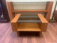 Front view of the teak side table showing smoked glass top and lower teak wood shelf.