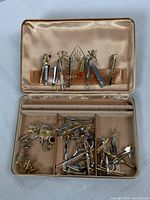 Image of open Farrington box containing assorted cufflinks in the lower compartment and tie-pins secured in the upper satin-lined lid holder.