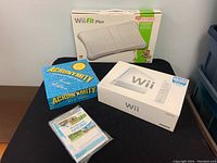Photo showing sealed Wii Fit Plus Balance Board box, Acronymity Trivia Edition board game, sealed Wii Sports game and manuals, and sealed Nintendo Wii console box.
