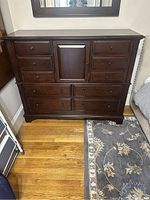 Full view of wooden dresser showing multiple drawers and cabinet door, dark brown finish on hardwood floor.