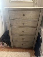 Front view of tall dresser showing curved front, marble top, and five drawers with knobs.