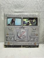 Front cover of Bob Marley & The Wailers "Babylon By Bus" album showing bus grille design with photos and globe graphic