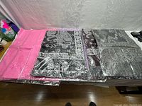 Seven scarves laid out on a flat surface, all in clear plastic packaging. Includes solid pink scarf and multiple patterned scarves in muted colors like black, grey, and brown.