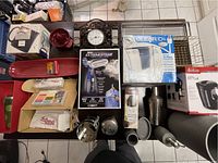 Overview of various household items including boxed steam iron, kettle box, beverage filter jug box, black clock, red kitchen bowls, and metal hooks.