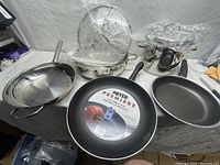 Overview of the lot with multiple pots and pans on display, some with lids covered in plastic wrap to protect them.