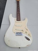 Front view of the guitar body showing white finish, three single coil pickups, control knobs, missing output jack