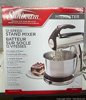 Photo of the sealed retail box showing Sunbeam Mixmaster 12-Speed Stand Mixer with product image and usage highlights.