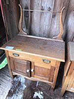 Front view of the antique wooden wash stand, showing top drawer with metal handles and lower cabinet doors with ceramic knobs.