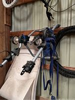 Side view of silver metal Thule bike rack with blue straps and black plastic bike clamps hanging on a wall.