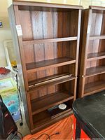 Front view of the tall wood laminate bookcase showing five shelves and wood grain pattern.