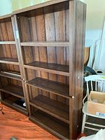 Full view of the tall wood laminate bookcase showing four shelves and dark wood grain finish. Visible wear and damage on corners and edges.