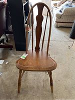 Front view of vintage wooden Windsor chair showing rounded seat, curved spindles, and visible scratches on finish.