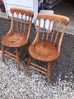 Front view of two wooden chairs with spindle backrest showing damage to seats and legs on gravel surface in front of garage