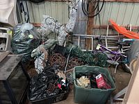 Photo showing bins, bags filled with Christmas decorations including a plant wreath, ornaments and garlands, partially visible green sled and white lighted reindeer figure.