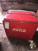 Front view of the red Coca Cola metal cooler with logo, showing wear and dirt.