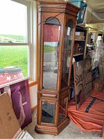 Full view of the wood curio cabinet showing its shape, finish, and glass panels.