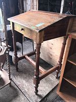 Front and side view of wooden desk showing slanted top surface, single drawer with wooden knob, turned legs, and stretcher supports.