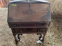 Front view of the wood secretary desk, showing drop front panel closed and legs, situated in a barn environment.