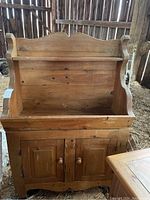 Front view of the wooden dry sink showing the upper shelf, scalloped top backboard, and two-door lower cabinet.