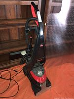 Front and side view of Bissell ProHeat floor finishing machine showing upright black and red body with solution tank and hose attached.