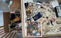 Wide view of assorted costume jewellery pieces with watches, earrings, bracelets, and pins laid out on a surface and loose in a box.