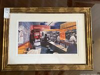 Framed and matted limited edition print by Les Tait hung or leaning, showing the gold-toned frame and matting around the print.