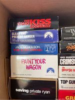 Box of VHS movies showing titles 'The Long Kiss Goodnight,' 'Clean and Present Danger,' 'The Last Detail,' 'Paint Your Wagon,' and 'Saving Private Ryan'