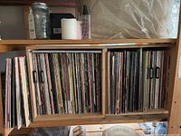 Two wooden shelves with vinyl LP records stored upright and miscellaneous items on top
