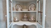 China cabinet shelves with stacks of plates, cups and saucers showing Canton pattern.