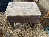 Front and side perspective view of the shoe shine box sitting on a hay floor, showing legs and overall structure.