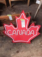 Front view of the red metal maple leaf sign with white LED tubing outlining the leaf shape and spelling 'CANADA'.