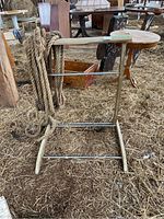 Photo showing the wood frame of the stand with horizontal metal bars and the thick rope draped over the top bar, placed on hay.