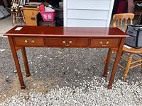 Full view of wooden console table with three drawers on gravel ground and garage background. Shows overall design and condition.