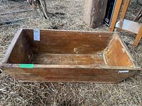 Front side angled view of the wooden trough placed on straw with visible wear and sticker labels.