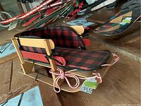 Side angled view of the vintage wooden sled showing wood finish, plaid cushion, and pink rope.