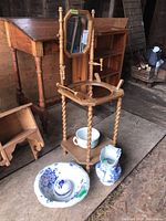 Antique wooden wash stand set including the cracked ceramic basin and accessories with blue floral pattern on ceramic pieces. The wash stand has twisted legs and a mirror attached at the back.